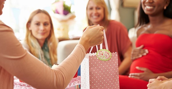 Women surround the party guest of honor and hand her gift bags.