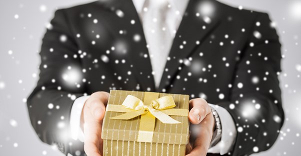 Man in a suit holds out a Christmas gift while snow falls
