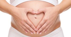A woman holds hands over her belly in the shape of a heart.