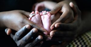 a couple holds hands around the feet of their baby in a pregnancy announcement