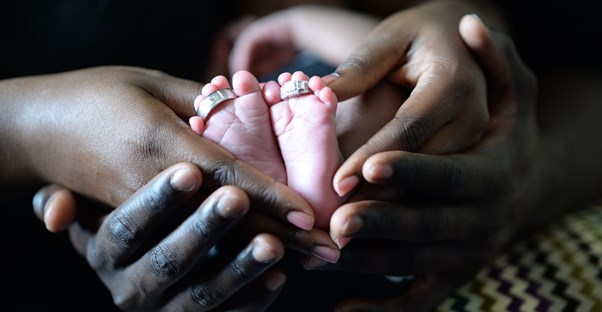 a couple holds hands around the feet of their baby in a pregnancy announcement