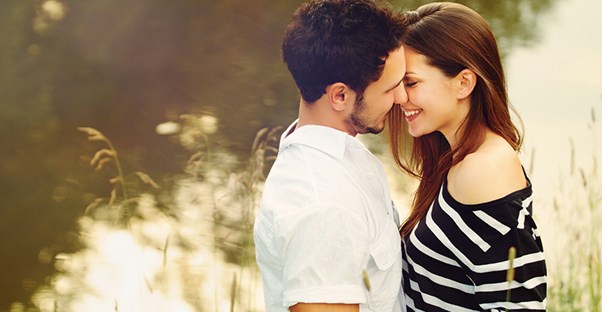 A young couple embraces in front of a scenic lake.