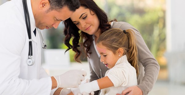 A pediatrician wraps a cast around the arm of a little girl