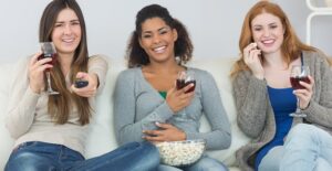 Three girls watch Scandal while eating popcorn and drinking red wine