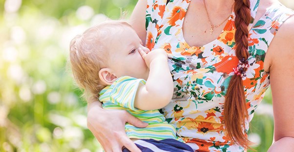A woman holds her son outside while breastfeeding.