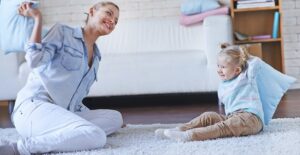 A babysitter and a toddler have a pillow fight
