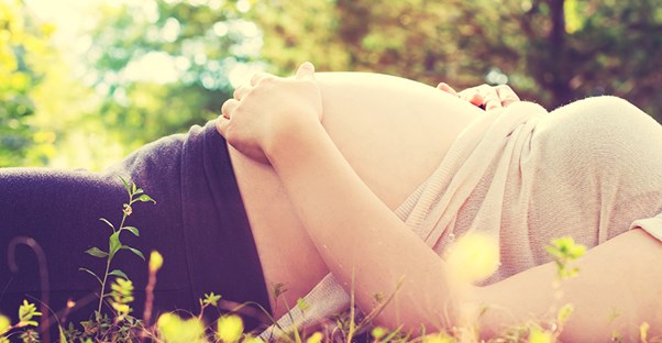 a woman hold her pregnant stomach while lying in a forest
