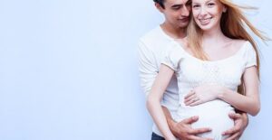 A young couple, the woman pregnant, embraces in a stylized windblown image.