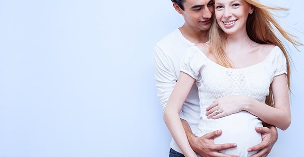 A young couple, the woman pregnant, embraces in a stylized windblown image.