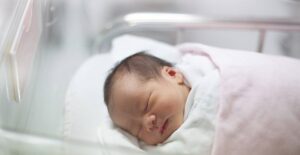 A newborn lies swaddled in a hospital nursery crib.