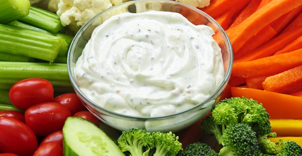 A bowl of ranch surrounded by veggies.