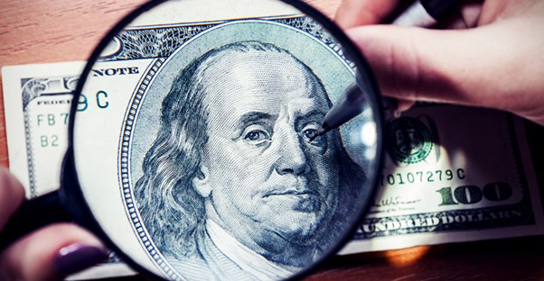Woman authenticating a hundred dollar bill with a marker and magnifying glass