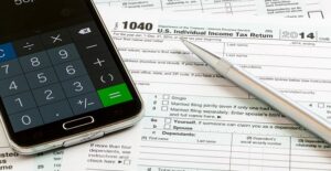 A stack of tax forms with a phone calculator and pen on top.