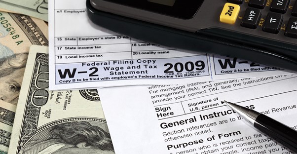 Money on a table covered with a W-4, calculator, and pen