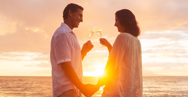 A retired couple is standing on the beach with glasses of champagne