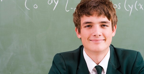 A young student wears a school uniform in front of a chalk board
