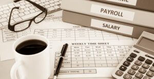 Stack of binders and payroll data on a desk with coffee