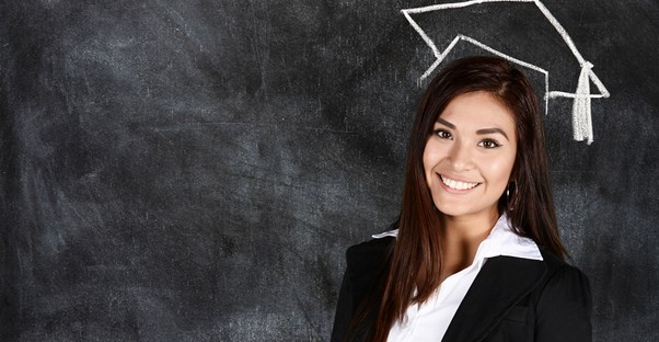 A girl poses under a drawing of a graduation cap on a blackboard