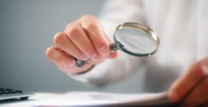 Teacher holds up a magnifying glass to a students paper to check for plagiarism