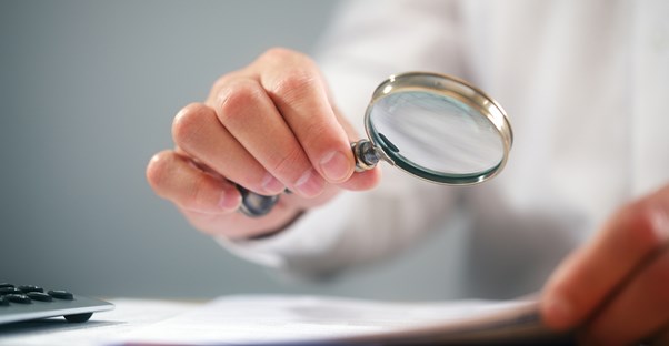 Teacher holds up a magnifying glass to a students paper to check for plagiarism