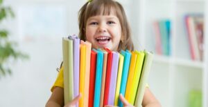 A young preschool girl carries school books in a classroom
