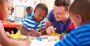 A preschool teacher colors with preschool students