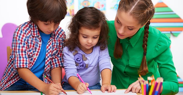 A preschool teacher helps her students draw