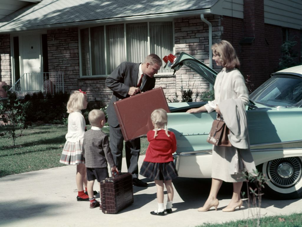 A classic 1950s scene of a dad coming home from work and being surrounded by his wife and kids by the car.