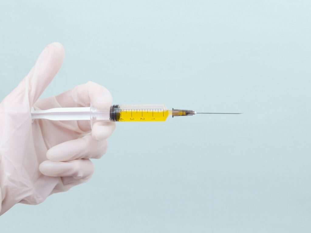 A doctor's hand in a white medical glove holds a syringe with a yellow medicine on a blue background