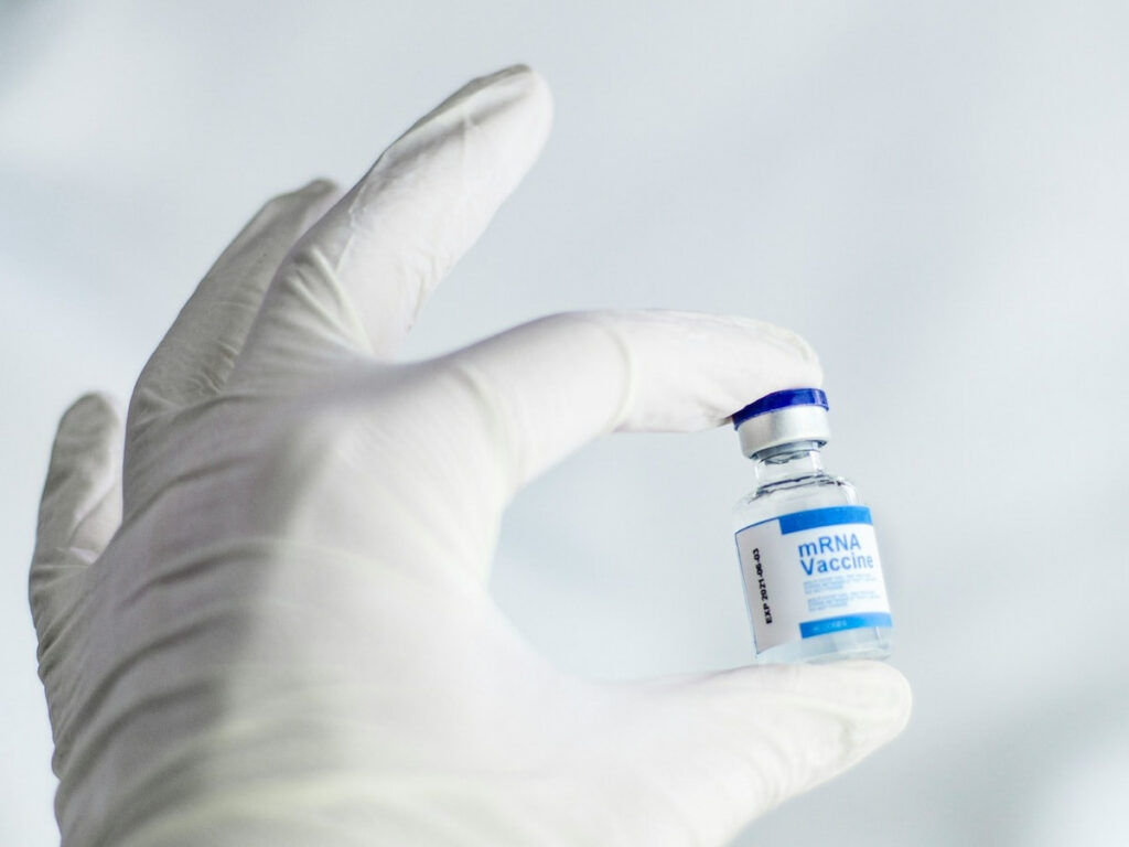 A doctor's gloved hand holding a white and blue MRNA vaccine vial.
