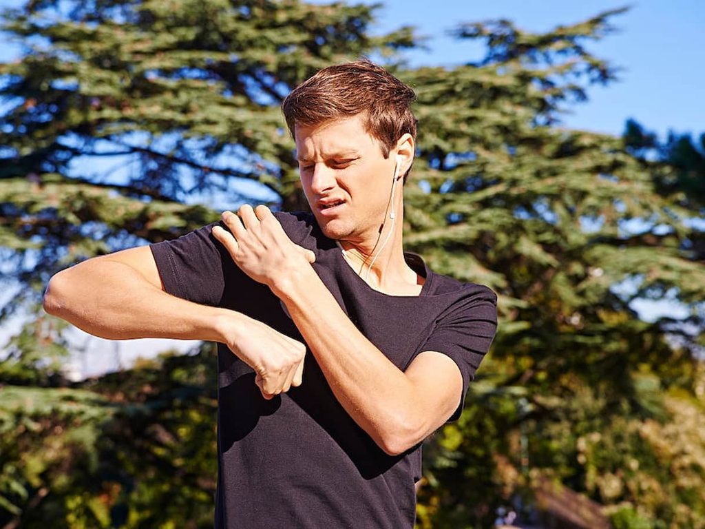 A young man grabs his shoulder in pain while on a run.