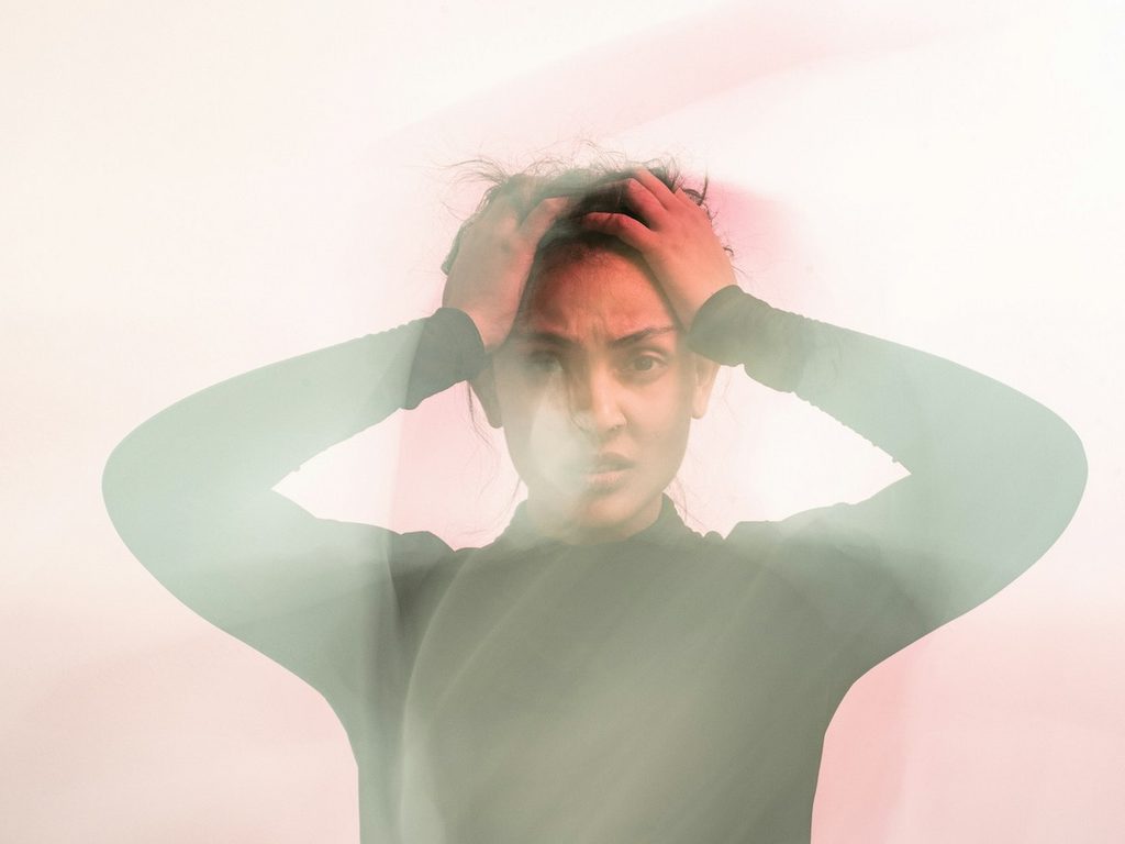 A woman in a gray turtleneck long sleeve shirt holding her head in confusion and frustration.