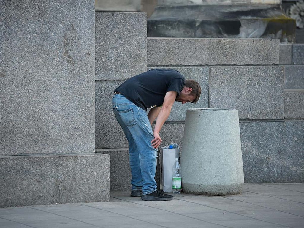 A nauseous man is seen bending over near a trash receptacle in Warsaw, Poland.