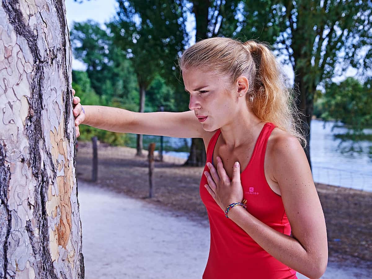 A woman leans against a tree after experiencing chest pain during a run.