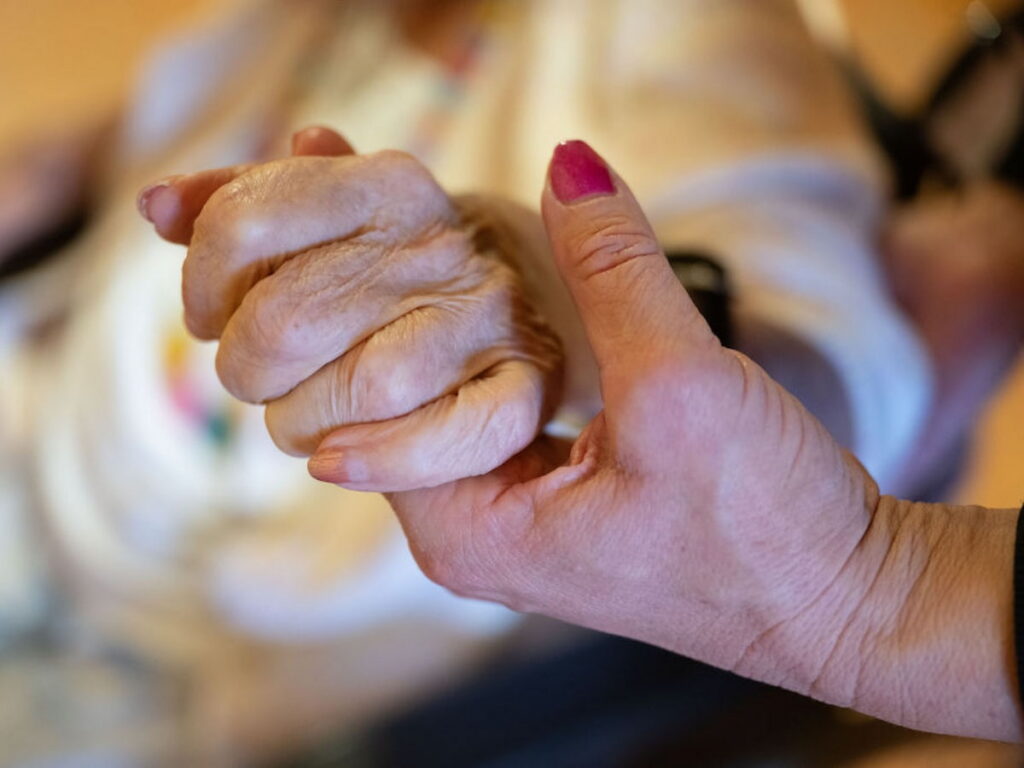 A physical therapist holds the hand and elbow of a nursing home resident.