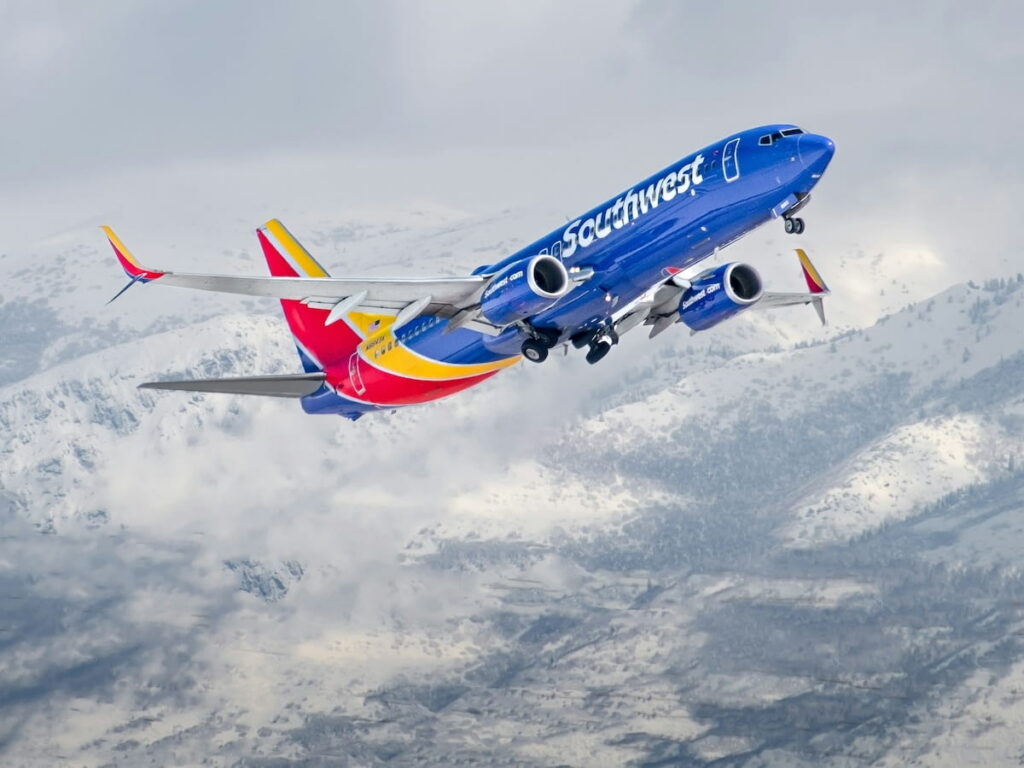 A Southwest Airlines plane taking off from Salt Lake City International Airport with snowy mountains in the background.